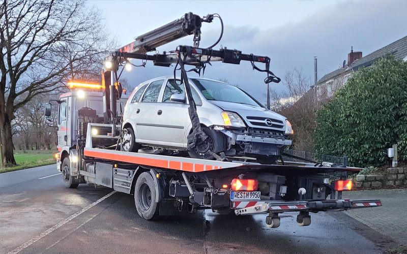 Abschleppwagen von AMF schleppt einen kleinen Opel auf der Ladefläche bei eingeschalteter Beleuchtung ab.